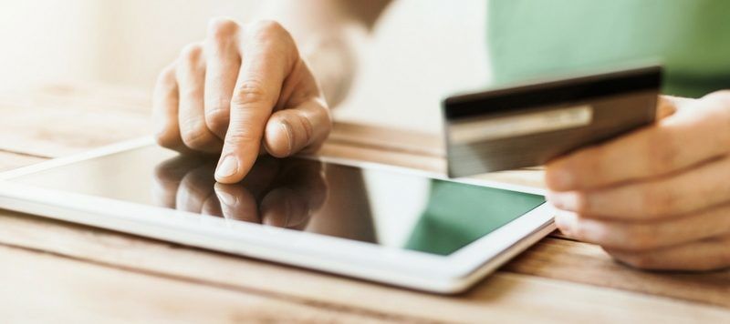 One Hand Holding a Credit Card and the Other Using a Tablet